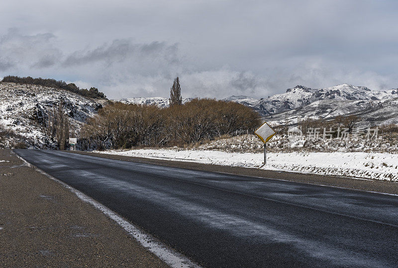 Ruta Nacional 237, RN237——下雪后的道路上有积雪，旁边有植被，沥青上有一些冰，指示牌被雪覆盖